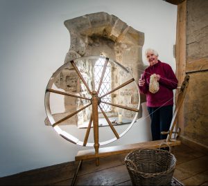 A female volunteer with wool by the spinning wheel
